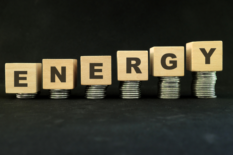 Letters spelling the word ’energy’ balanced on top of increasingly larger piles of coins